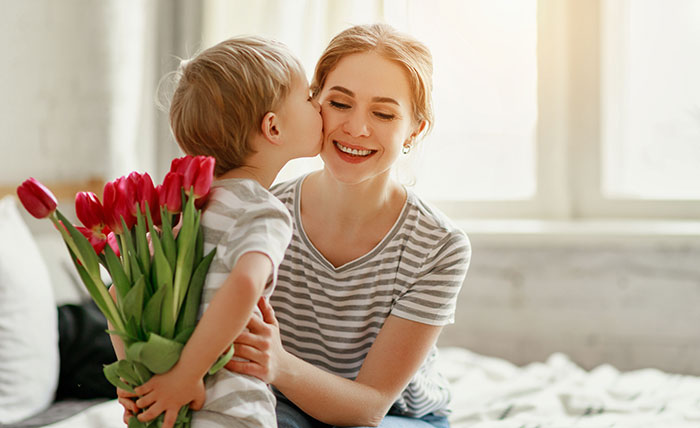 The baby is giving rose flowers to his mother.